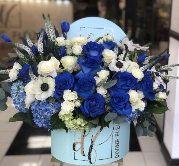 custom dyed blue roses are stunning, set along with blue hydrangea, blue tulips, and perfect white with a blue center Anemone and Veronica are arranged in a classic hat box style