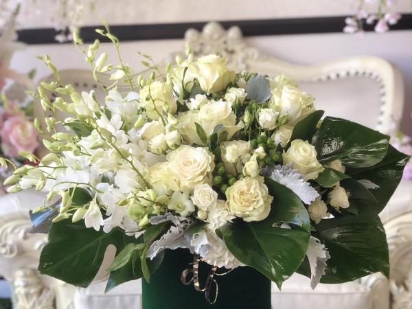 Emerald tropical leaves are the background to this white and green arrangement. Overflowing with Orchids, rich white roses, green coffee bean and spray roses, made in a Emerald green velvet keepsake box.
