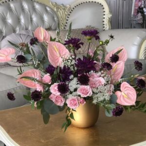 Pink anthurium accented with true purple dahlias and pink spray roses in a golden tone keepsake vase.