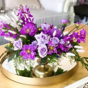 Purple Mokara orchids, purple Dahlias, lavender roses, and dark purple veronica, made in a beautiful golden tone pedestal vase.