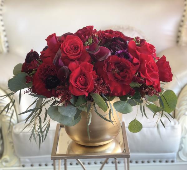 Red roses set in black Calla Lilies and burgundy Dahlias arranged in a modern gold vase
