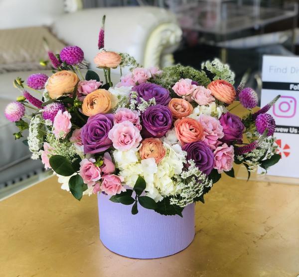 Summer bright mix of Mango ranunculus, Cool Water roses, fancy purple Dahlias, hydrangea Queen Ann's lace, spray roses, and Veronica arranged in a keepsake Lavender hat box